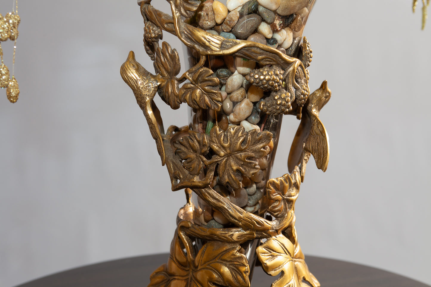 Close up view of ornate vase with leaves, flowers and pebble.