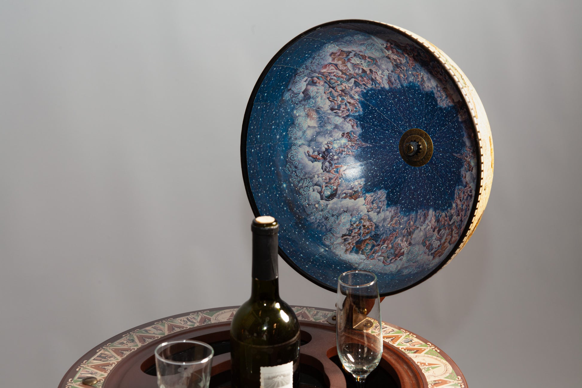 Open celestial globe with starry interior, wine, and glasses