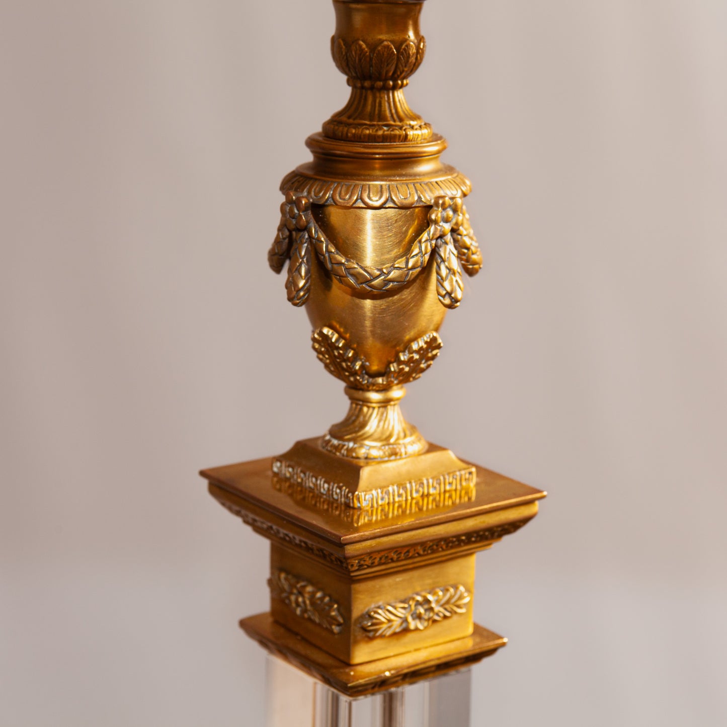 A close-up of an ornate gold lamp base with intricate detailing and decorative garland accents.