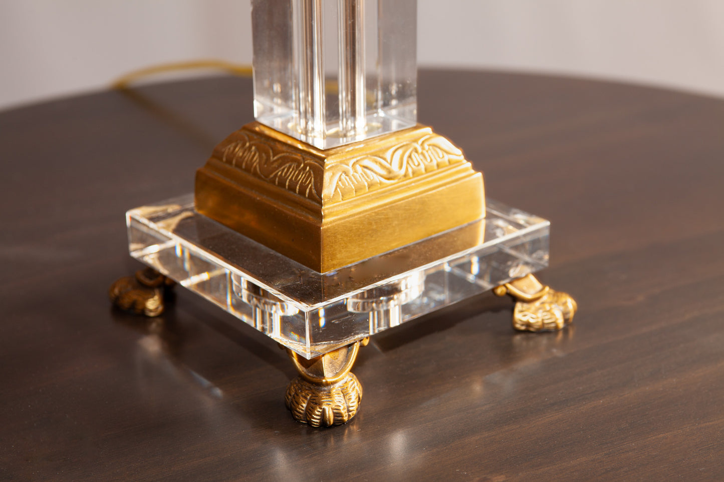 A close-up of a lamp base with gold detailing, a clear acrylic platform, and ornate clawfoot legs.