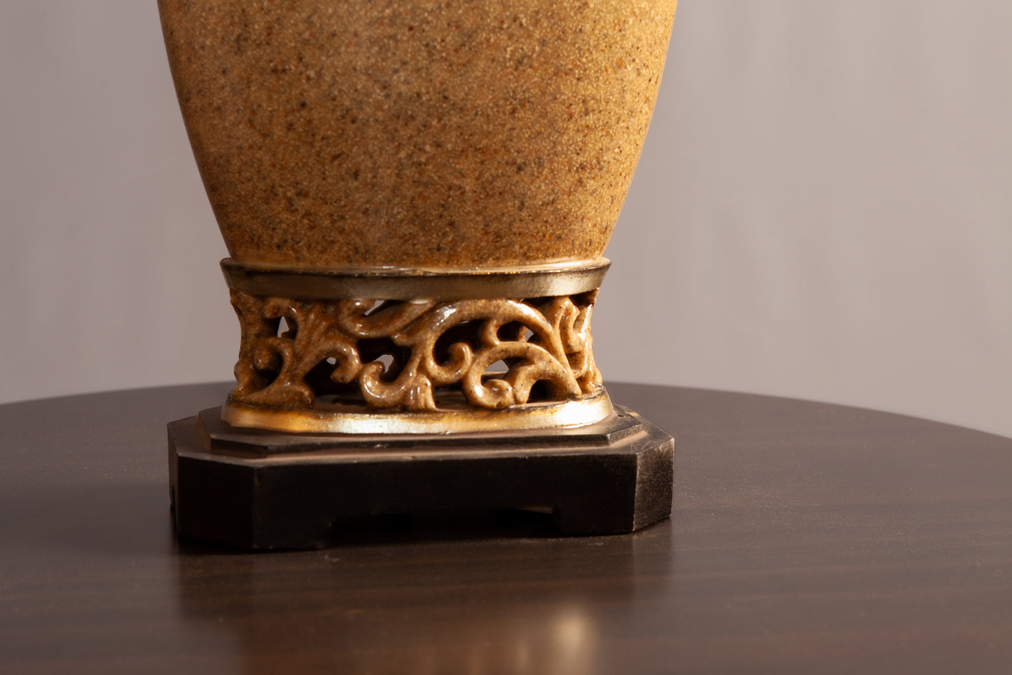 A close-up of a decorative lamp base with ornate gold scrollwork and a dark wooden platform