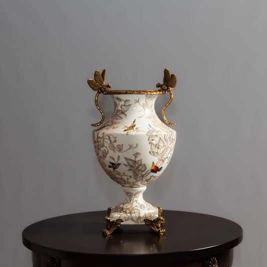 A decorative porcelain vase with gold butterfly handles and painted birds sits on a dark wooden table.