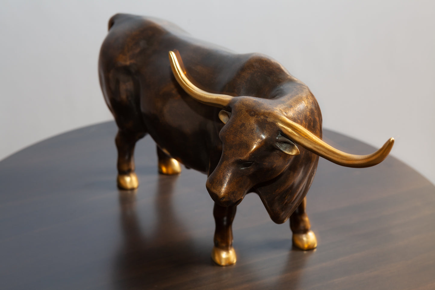 Top view of bronze bull with gold tip horn standing on a round brown table.