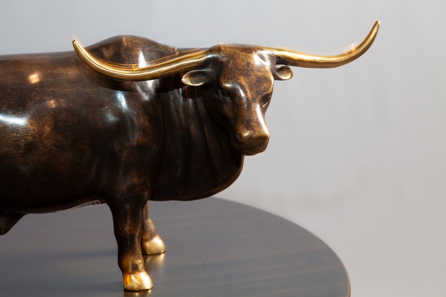 Close up view of bronze bull with gold tip horn standing on a round brown table.
