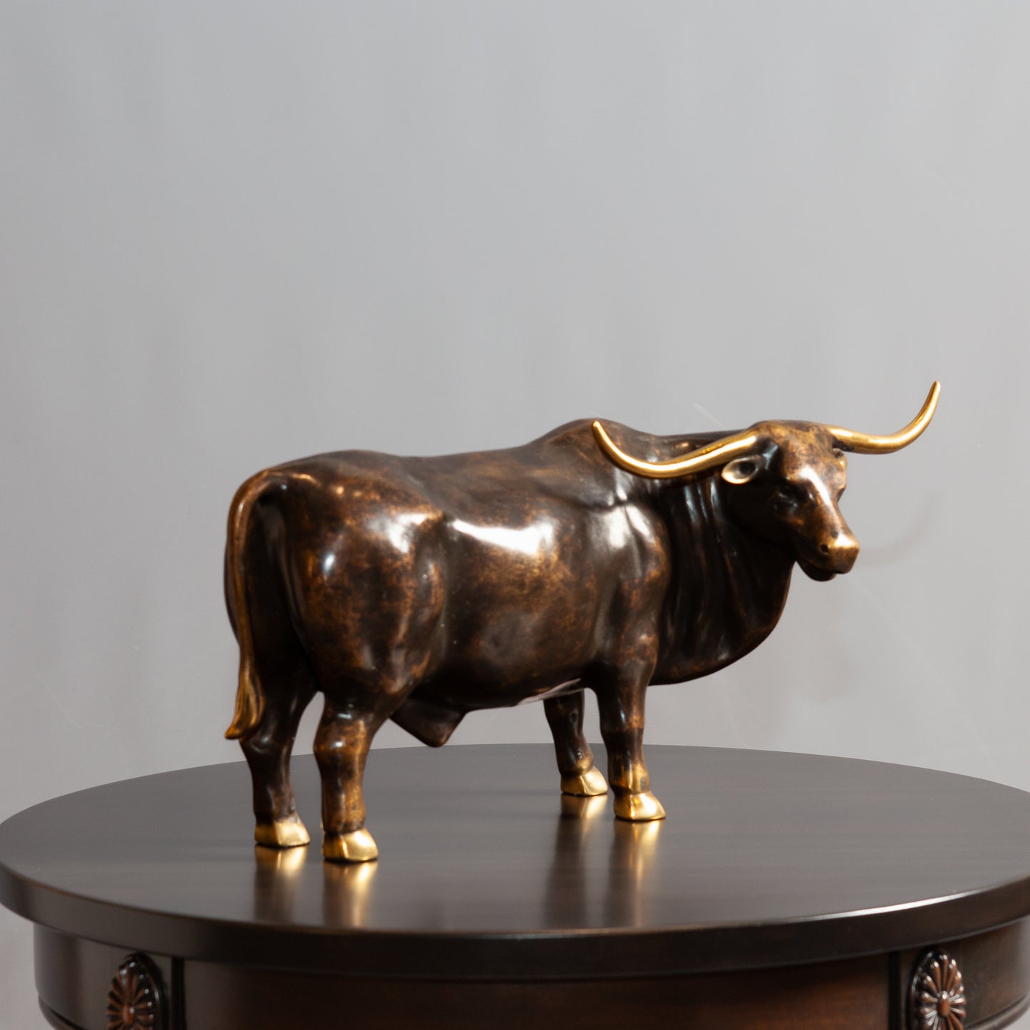 Side view of bronze bull standing on a round brown table.