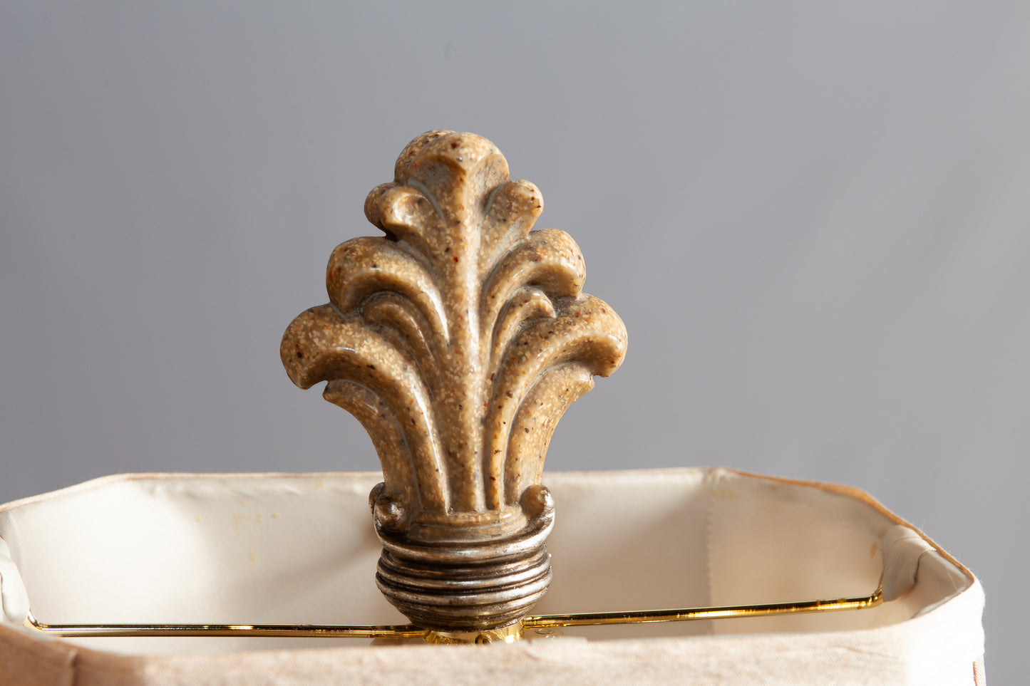 A close-up of an ornate finial with a carved floral design on top of a beige lampshade