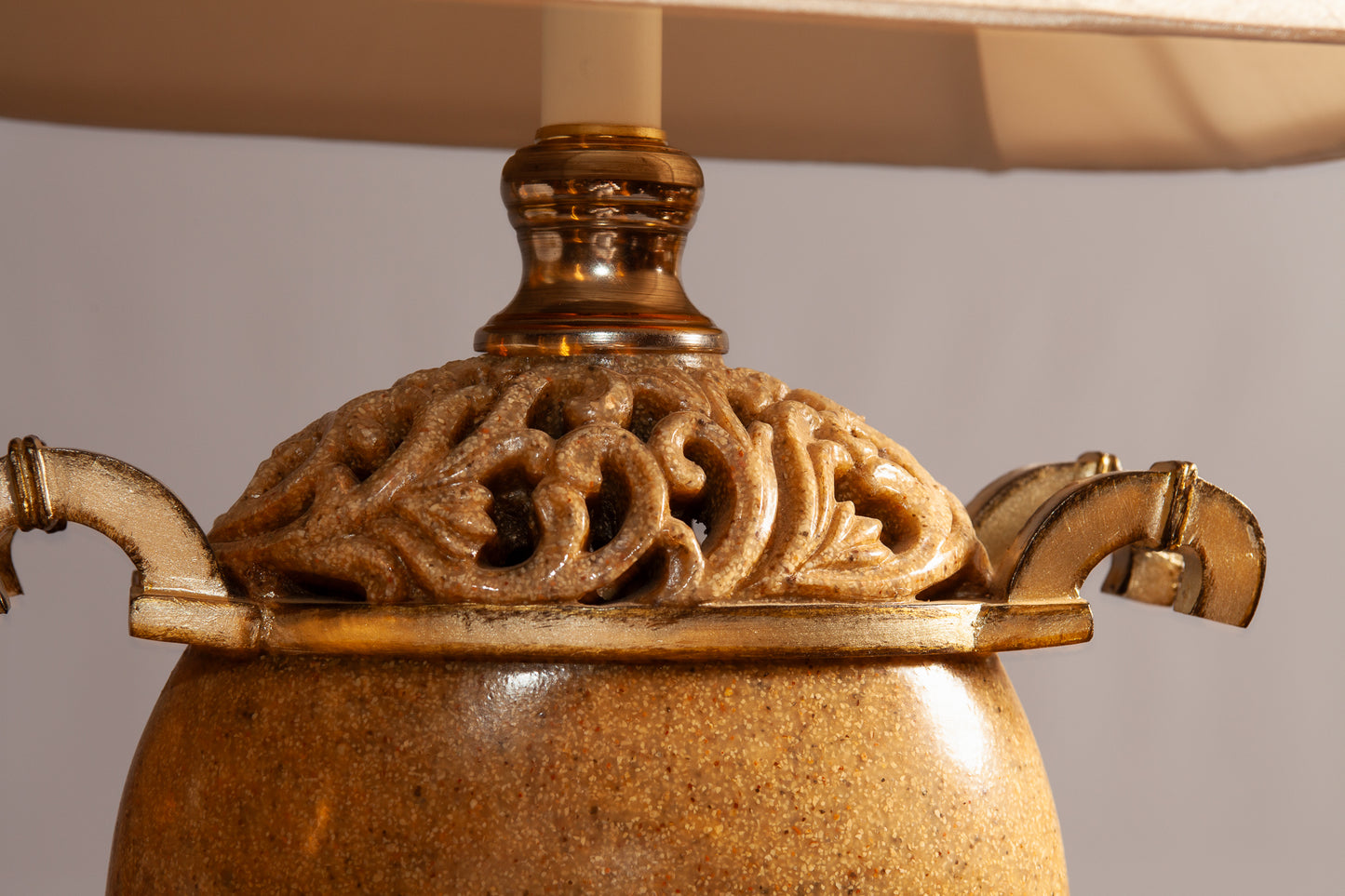 A close-up of an ornate gold and beige lamp base with intricate carved detailing and curved handles.