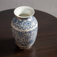 A blue and white porcelain vase with floral patterns and a wide rim sits on a dark wooden table.