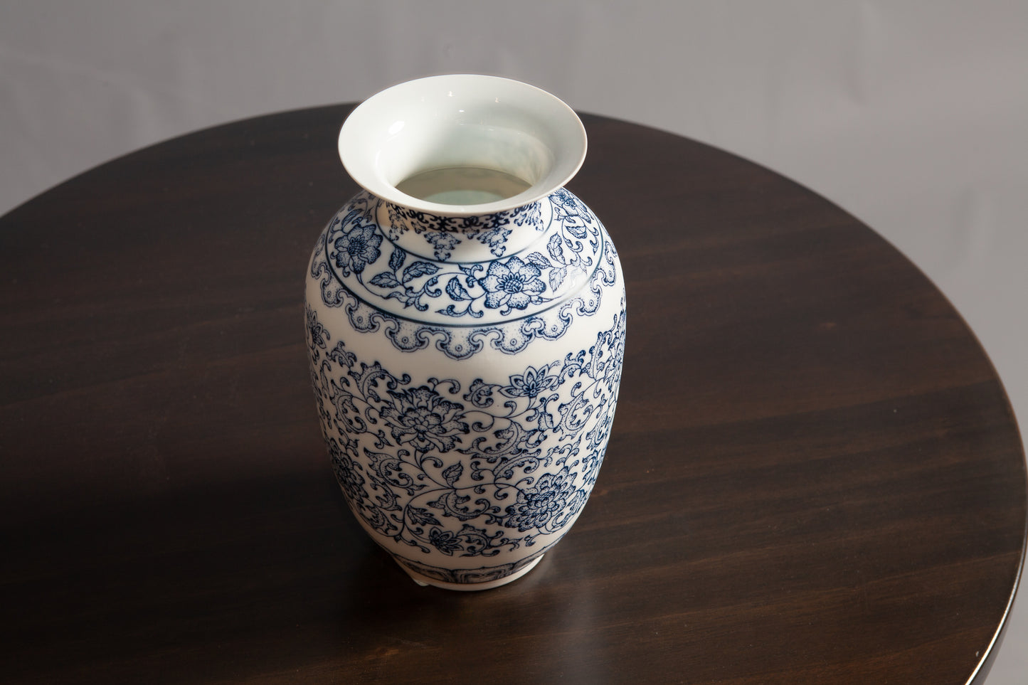 A blue and white porcelain vase with floral patterns and a wide rim sits on a dark wooden table.