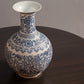 A blue and white porcelain vase with intricate floral and geometric patterns sits on a dark wooden table.