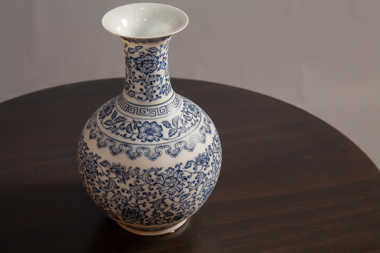 A blue and white porcelain vase with intricate floral and geometric patterns sits on a dark wooden table.