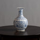 A blue and white porcelain vase with intricate floral patterns sits on a dark wooden table.