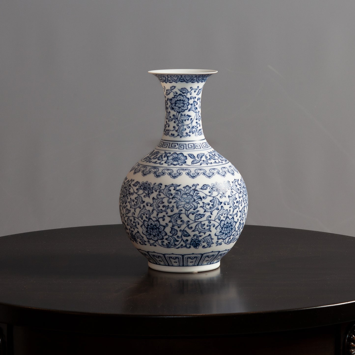 A blue and white porcelain vase with intricate floral patterns sits on a dark wooden table.