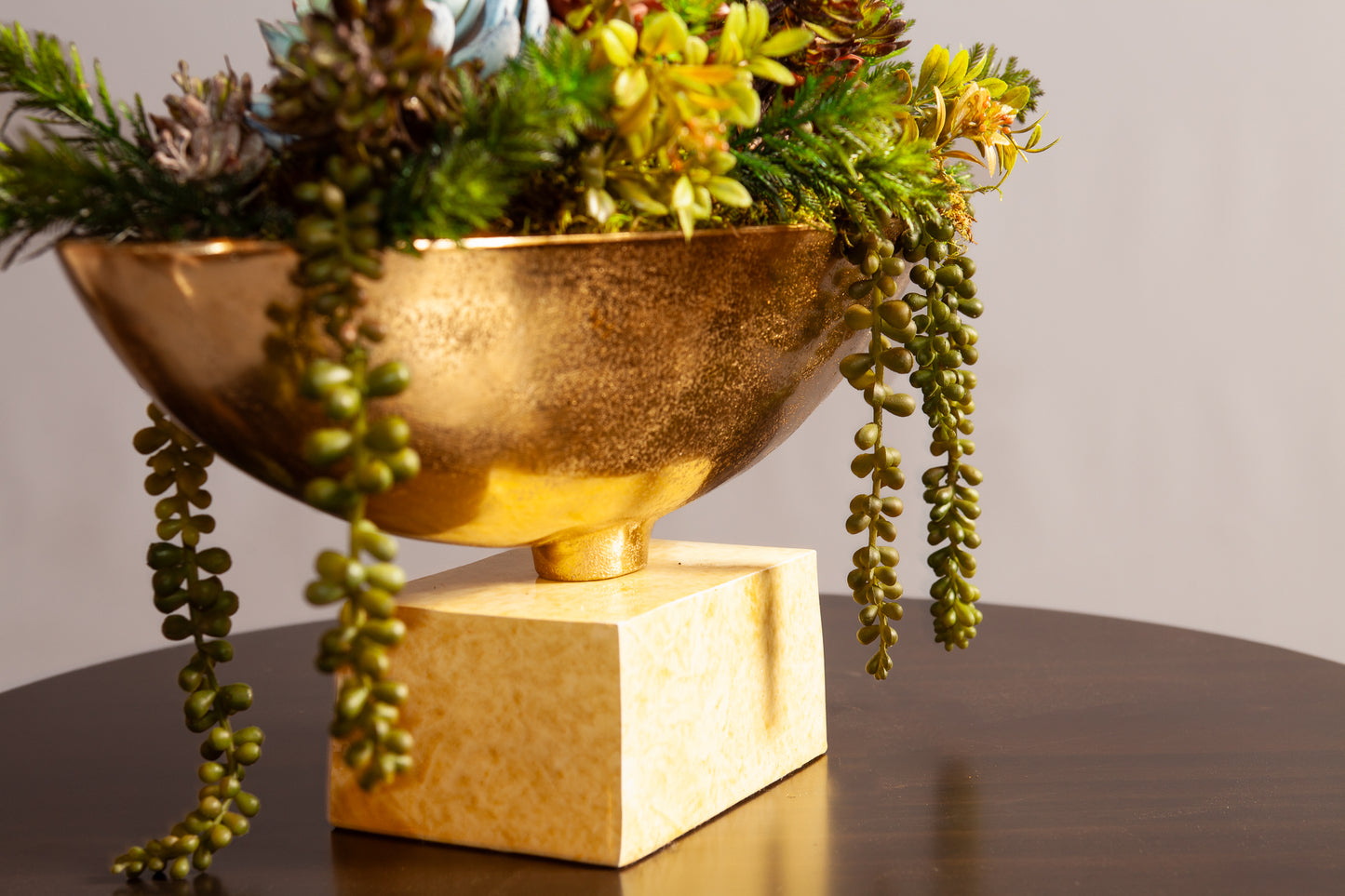 Close up view of decorative bowl with vibrant succulents and greenery sits on a dark wooden table.