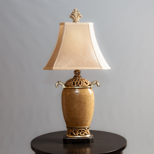 A gold and beige decorative table lamp with an ornate base and fabric shade